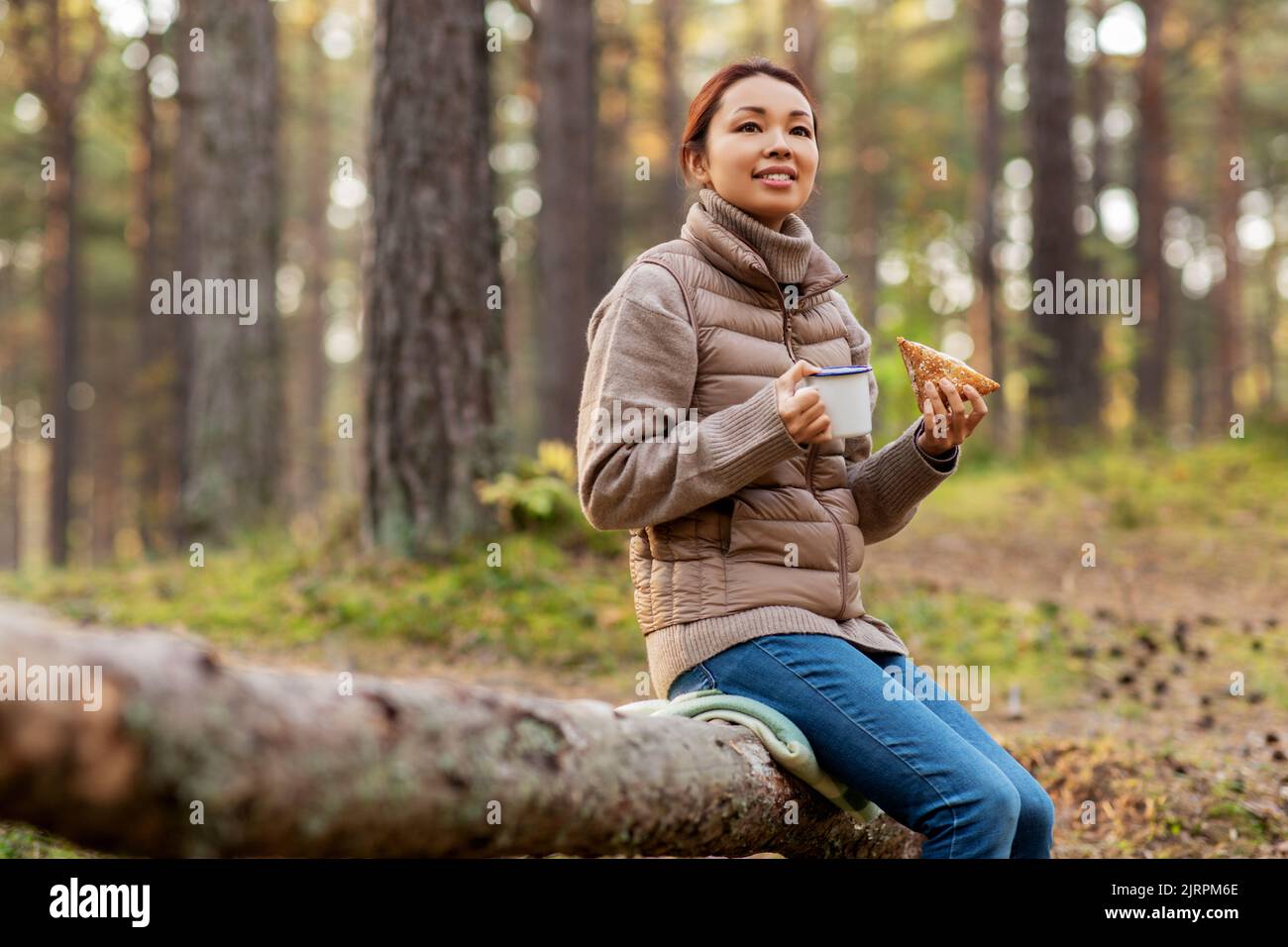 Frau trinkt Tee und isst Sandwich im Wald Stockfoto