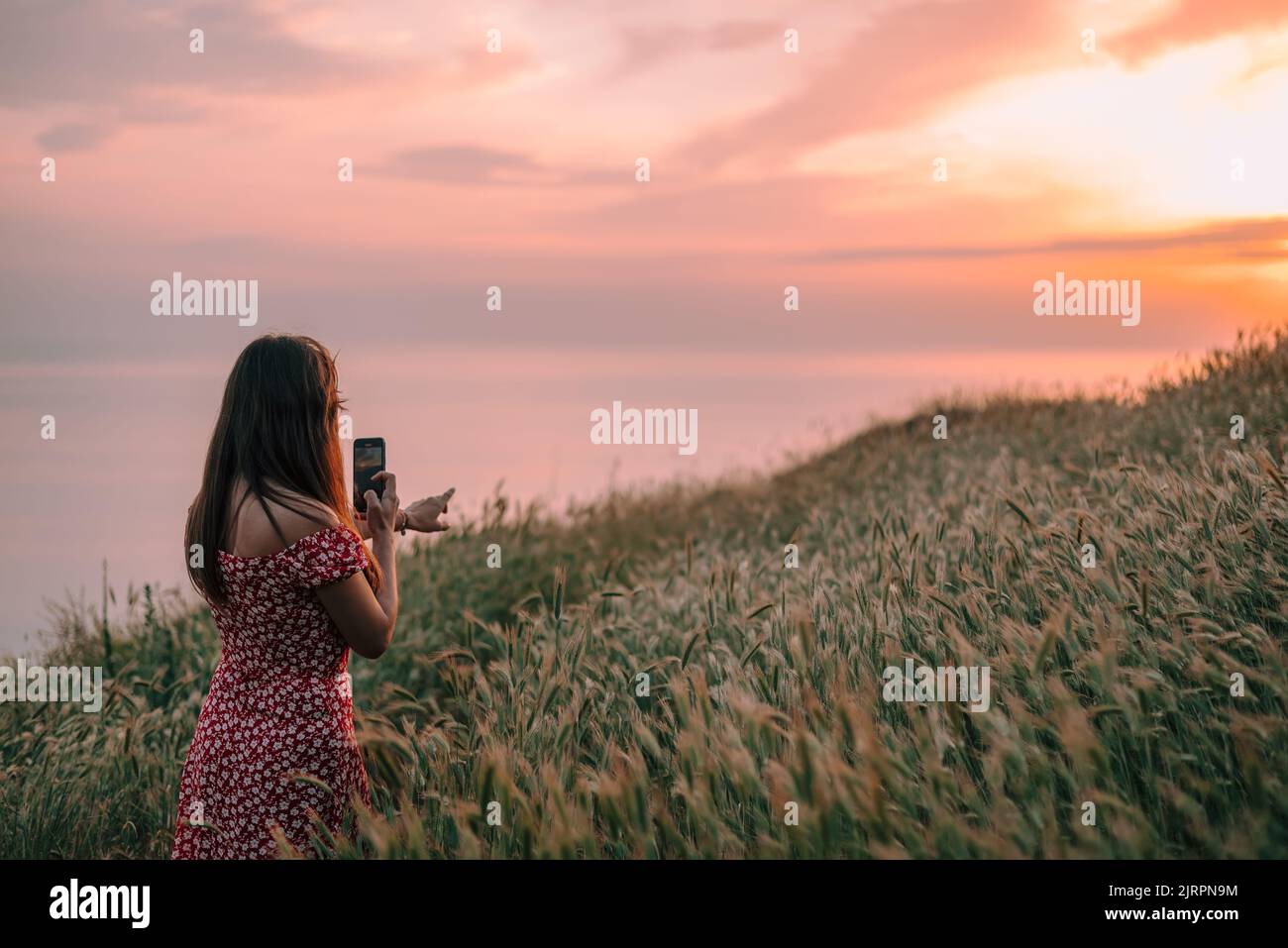 Junge Frau, die mit einem Smartphone einen Sonnenuntergang in den Bergen filmt Stockfoto