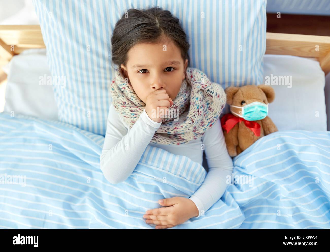 Krankes hustendes Mädchen mit Teddybär im Bett liegend Stockfoto