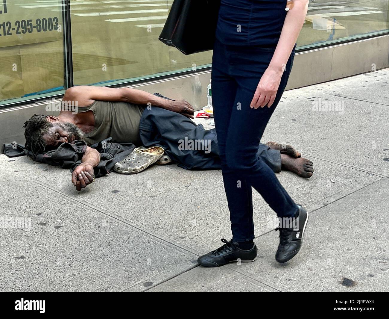 Obdachloser in wirklich schlechtem Zustand schläft auf dem Bürgersteig in der 32. Street in der Nähe der 7. Avenue in Manhattan, New York City. Stockfoto