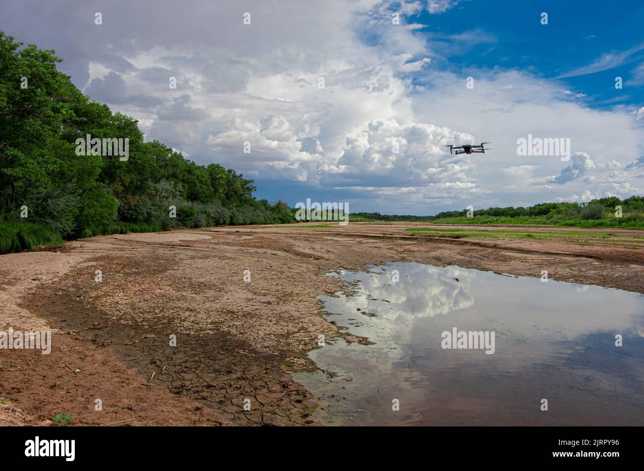 Ausgetrocknetes Flussbett mit Drohne, die über den Gipfel fliegt, mit Wolken und blauem Himmel in der Ferne und grünen Bäumen am Rand des ausgetrockneten Rio Grande Stockfoto