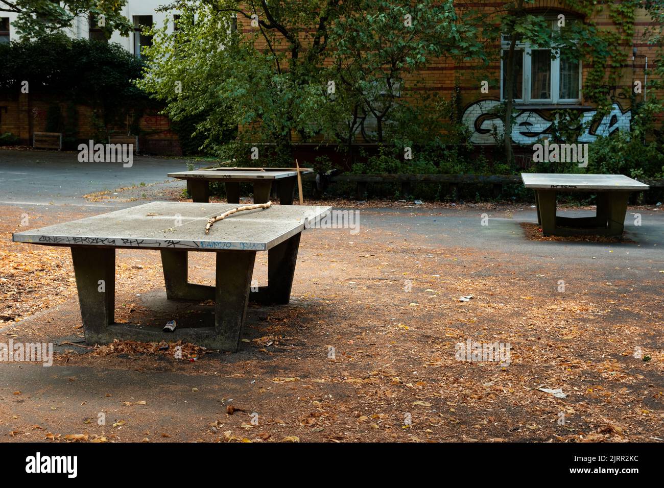 Verlassene Tischtennisplatte in einem alten Schulspielplatz. Kaputte Tischtennisplatte mit einem Ast oben. Gebäude in einer schlechten Gegend für Freizeit. Stockfoto