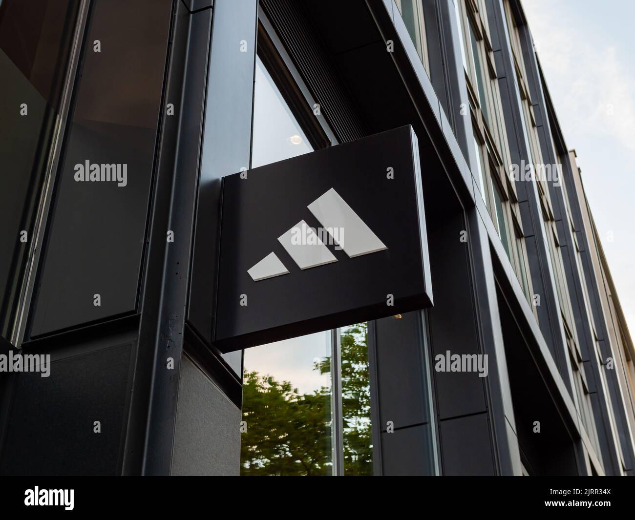 Adidas-Logo auf dem Äußeren eines Gebäudes. Eine große deutsche Modemarke für Schuhe und Sportbekleidung. Zeichen der bayerischen Firma auf einer Gebäudefassade. Stockfoto