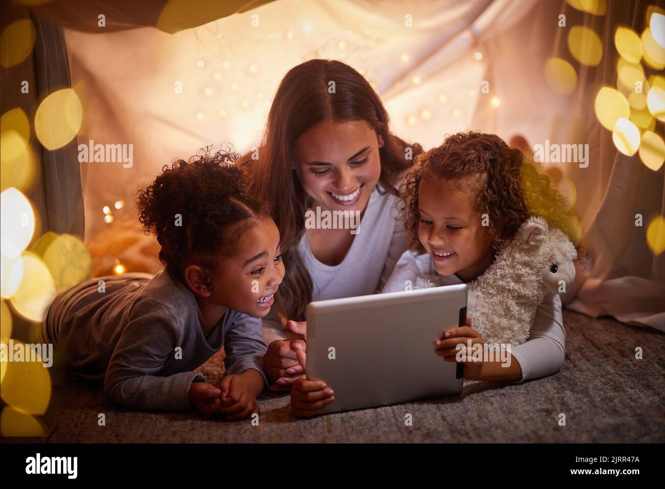 Mutter und Kinder streamen Live-Filme auf Tablet oder digitale Kinder-App in einem Zeltlager in der Nacht und Bokeh-Lichter. Pflege, liebe Mutter lesen ebook zu Stockfoto