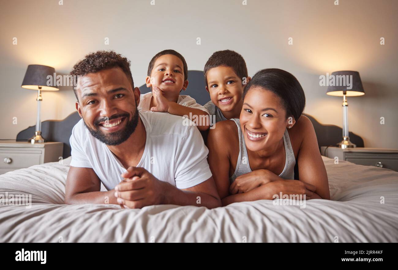 Porträt einer glücklichen schwarzen Familie auf einem Bett mit Kindern, sorglos, entspannend und spielend in einem Schlafzimmer zusammen. Junge Eltern genießen die morgendliche Bindung Stockfoto