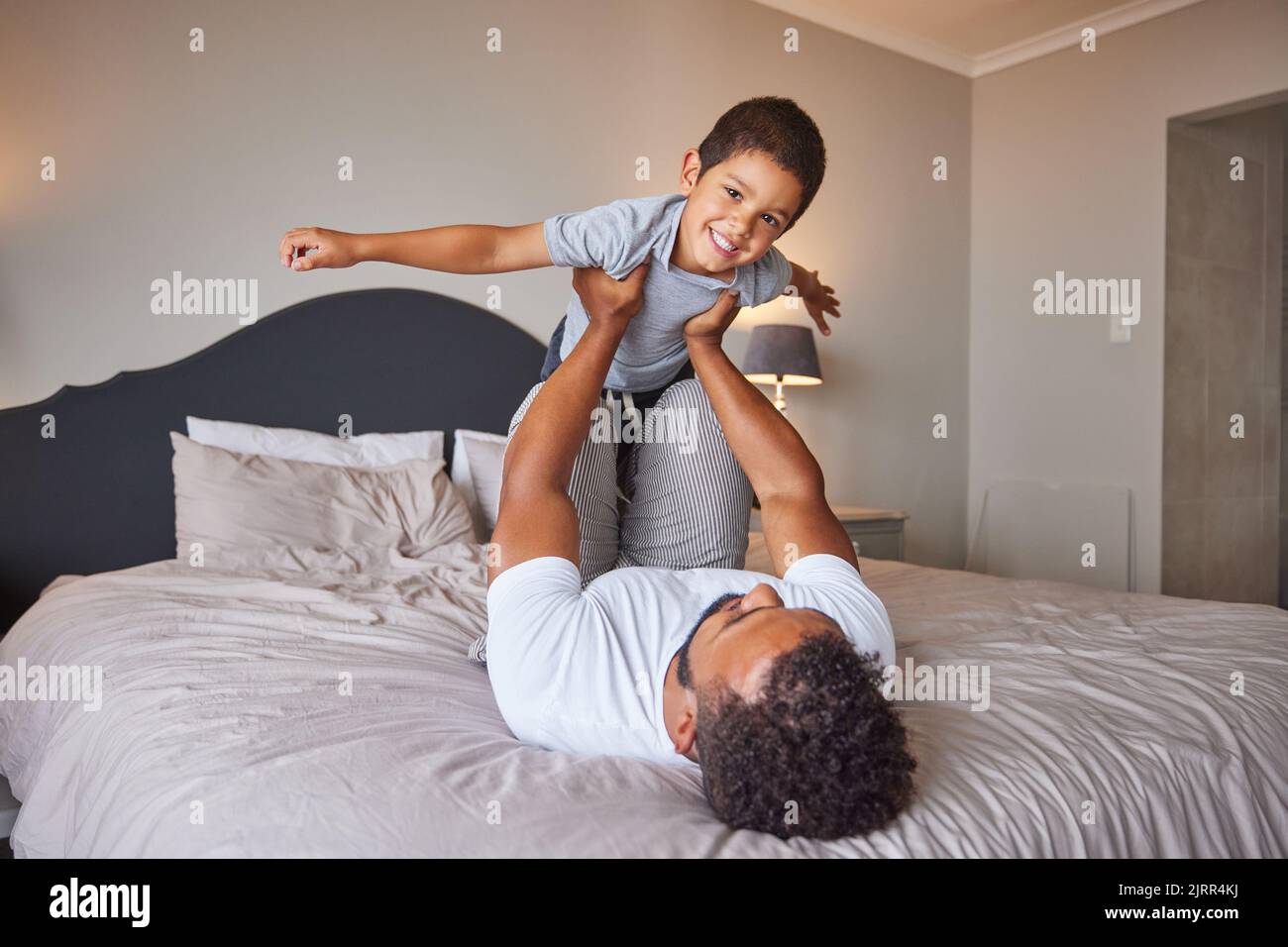 Lächeln, lieben und glücklich Vater und Sohn Familie Zeit spielen im Schlafzimmer Bett heben ihn wie Flugzeug oder Superheld. Liebevoller Vater, Mann oder alleinerziehender Elternteil Stockfoto