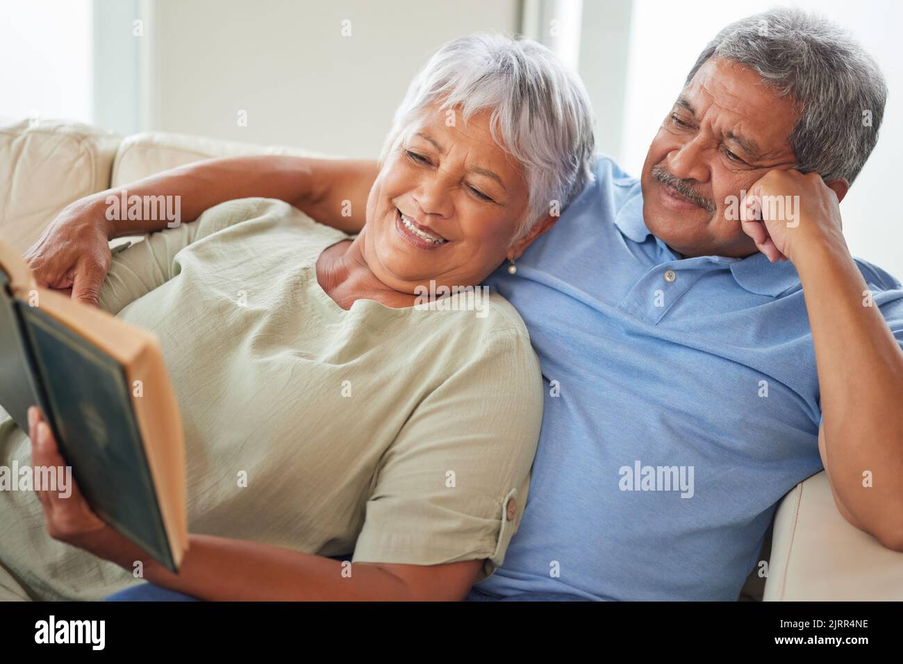 Entspannen Sie sich, ein glückliches und älteres Paar, das zu Hause ein Buch liest, während Sie sich auf der Couch entspannen und lächeln. Ältere oder alte Liebhaber lernen und ruhen sich aus Stockfoto