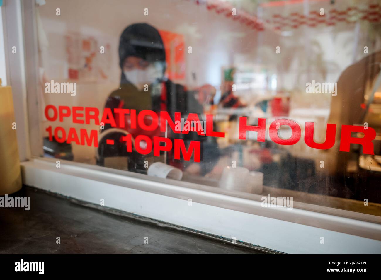 Die Betriebszeit des Restaurants wird im Kassenfenster mit weiblicher Mitarbeiterin im Hintergrund angezeigt Stockfoto