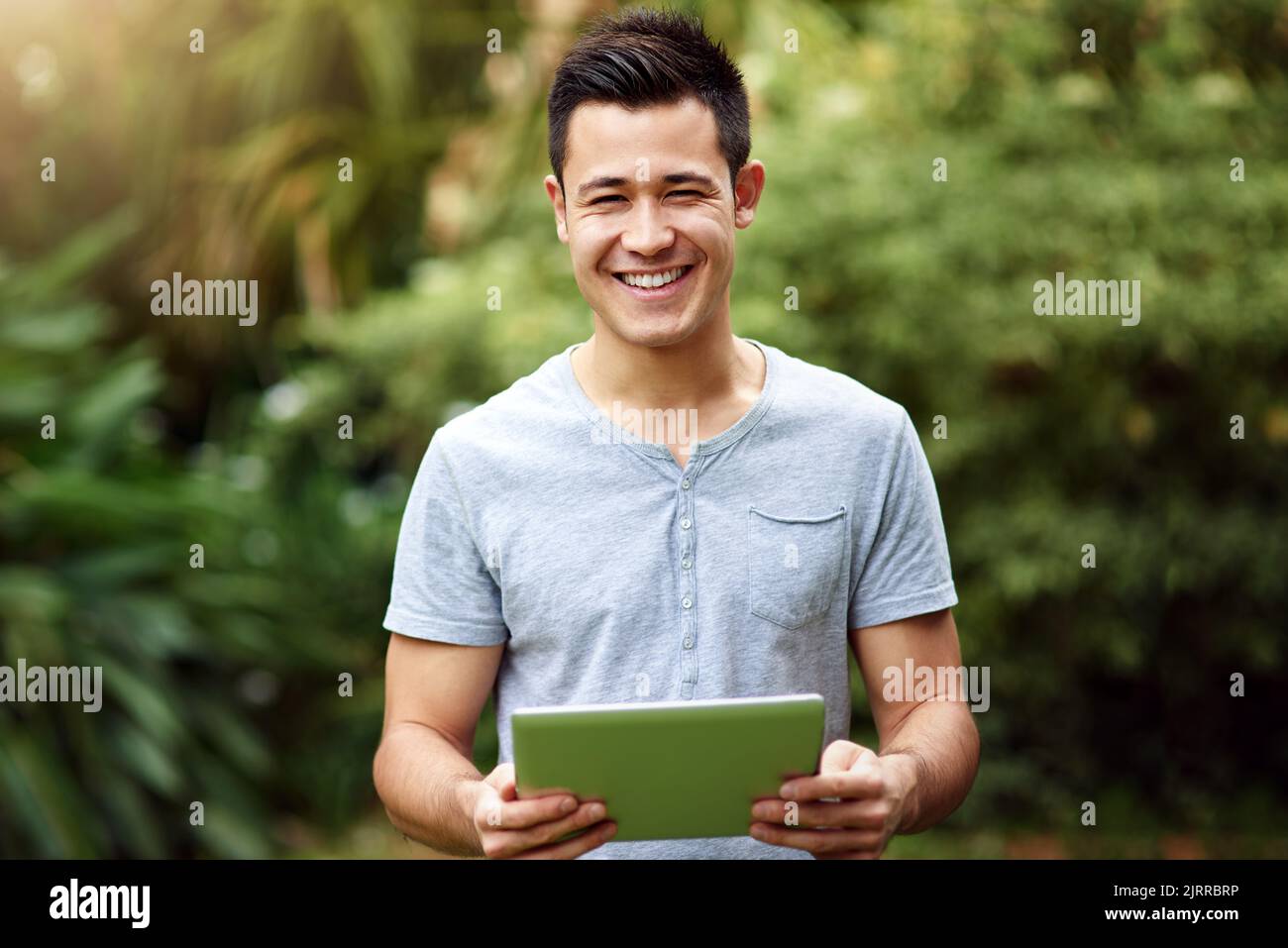 Mit Social Media durch den Park schlendern. Porträt eines hübschen jungen Mannes, der draußen ein digitales Tablet benutzt. Stockfoto