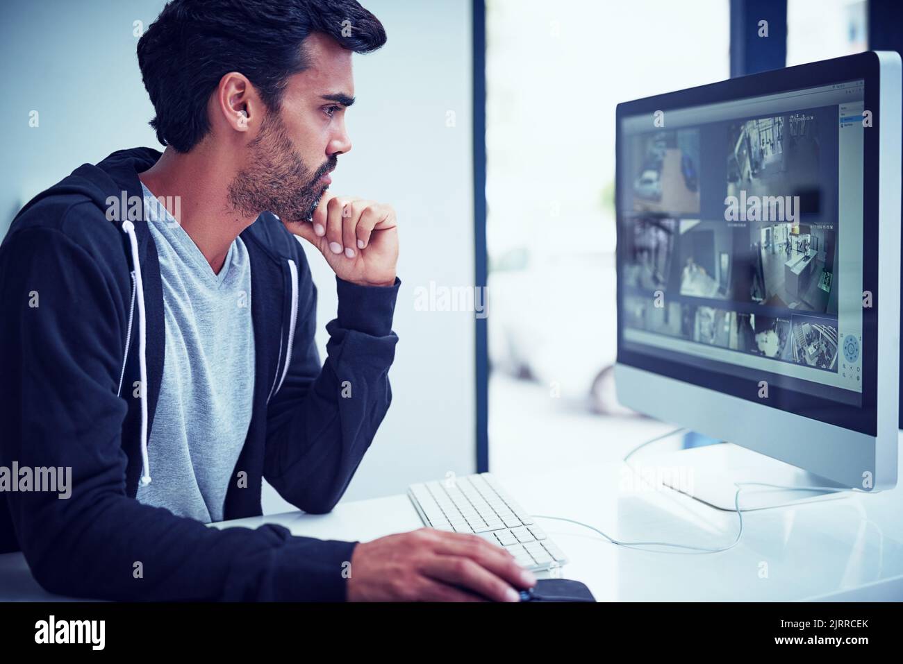 Ein junger Mann, der sich Sicherheitsaufnahmen auf seinem Computer ansieht. Stockfoto