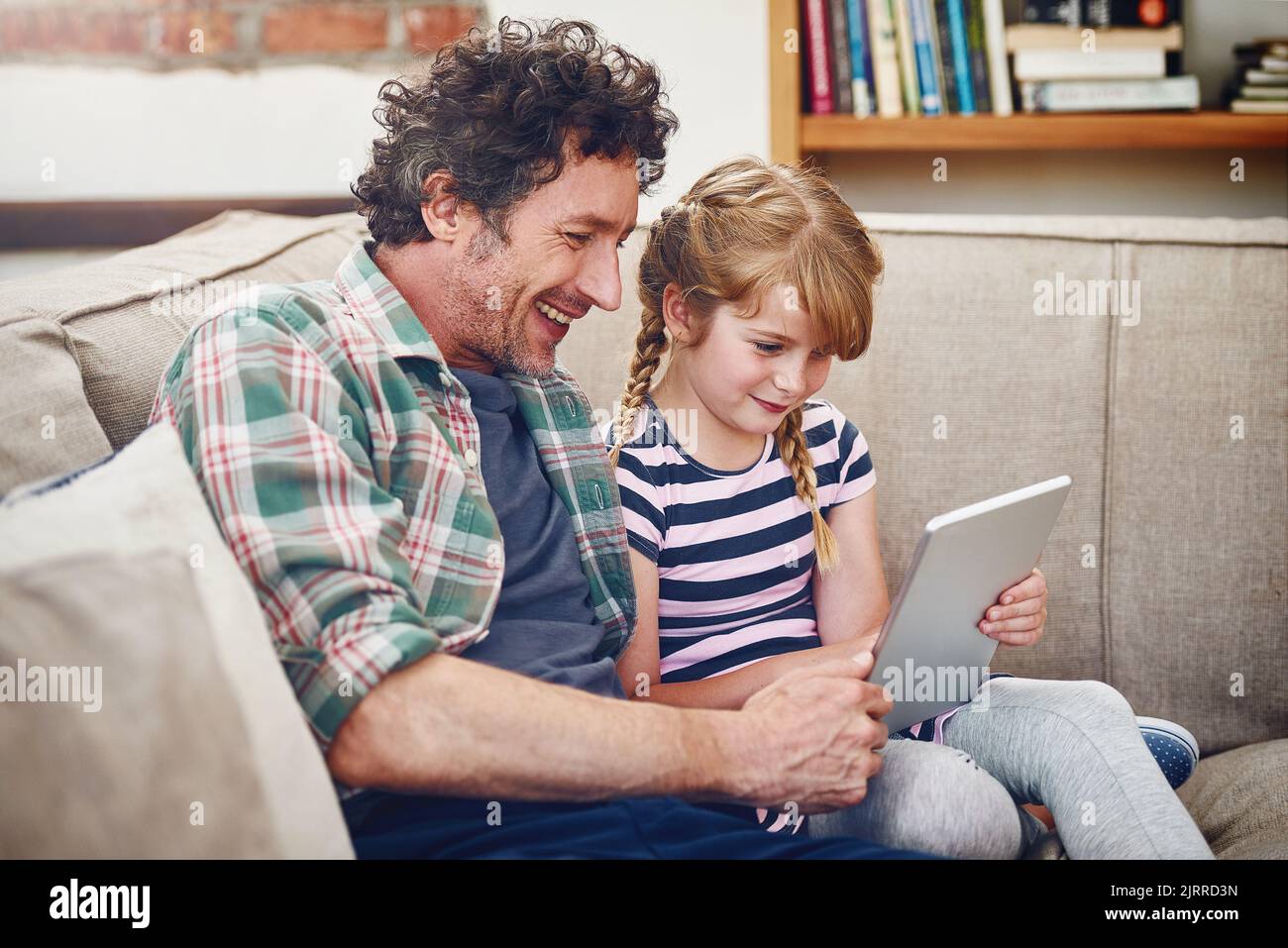 Mal sehen, ob ich meine Highscore schlagen kann. Ein Vater und seine kleine Tochter mit einem digitalen Tablet zu Hause. Stockfoto