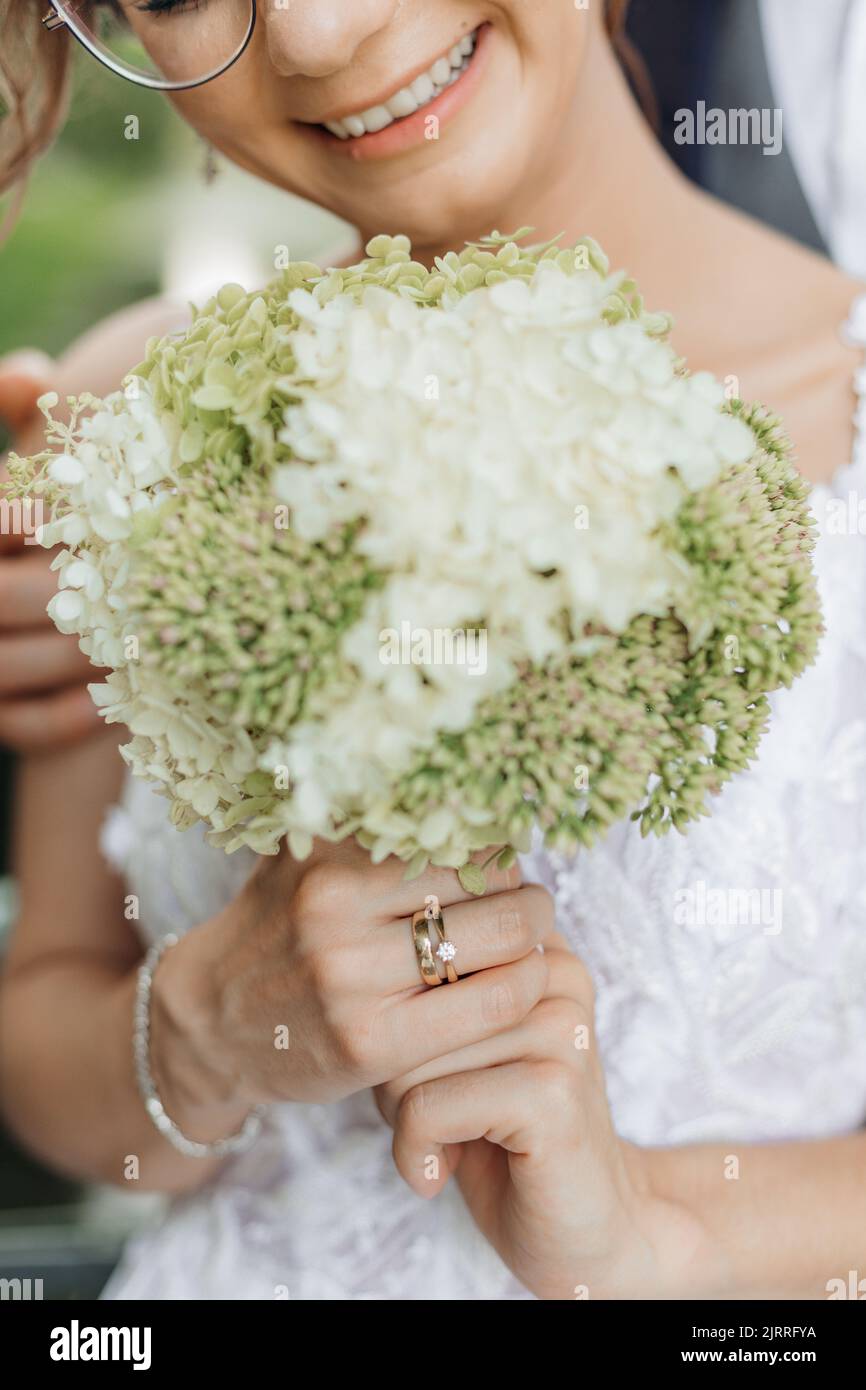 Nahaufnahme vertikaler Hochzeitsstrauß aus weißen und grünen Feldblumen in zugeschnittenen, nicht erkennbaren lächelnden weiblichen Brauthänden Stockfoto