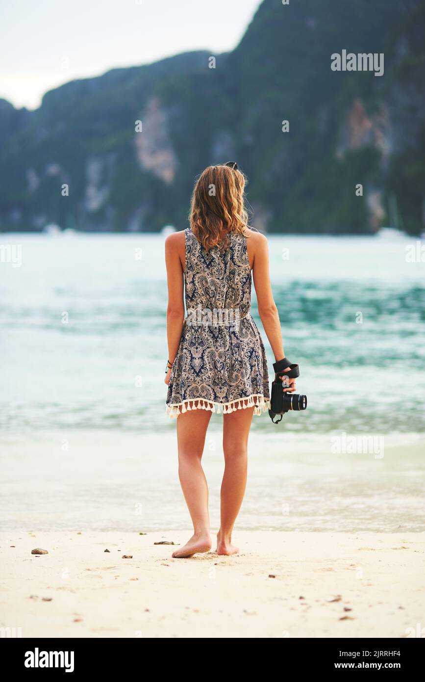 Mit einer Kamera in der Hand die Welt erkunden. Rückansicht einer jungen Frau, die mit einer Kamera in der Hand am Strand läuft. Stockfoto