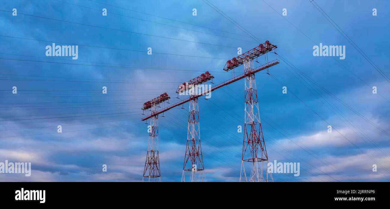 Hochspannungsleitungen und Strommasten bei Sonnenuntergang. Landschaft mit Wolken und blauem Himmel. Stockfoto