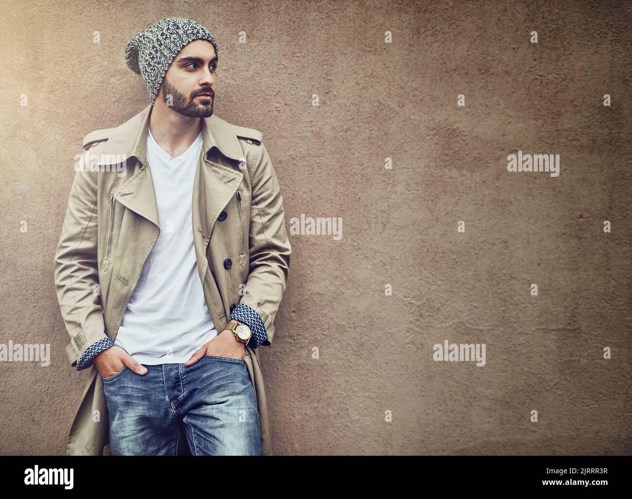 Nichts rundet den Streetwear-Stil ab als Swag. Ein modischer junger Mann, der urbane Kleidung trägt und vor einer braunen Wand posiert. Stockfoto