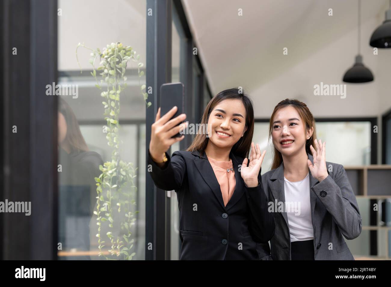Zwei asiatische Geschäftsfrau winken die Hände, um den Partner während einer Videokonferenz mit ihrem Team zu begrüßen. Stockfoto