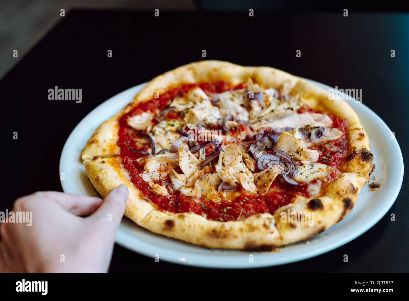 Hand nimmt eine Scheibe Pizza mit Huhn von einem Teller. Stockfoto