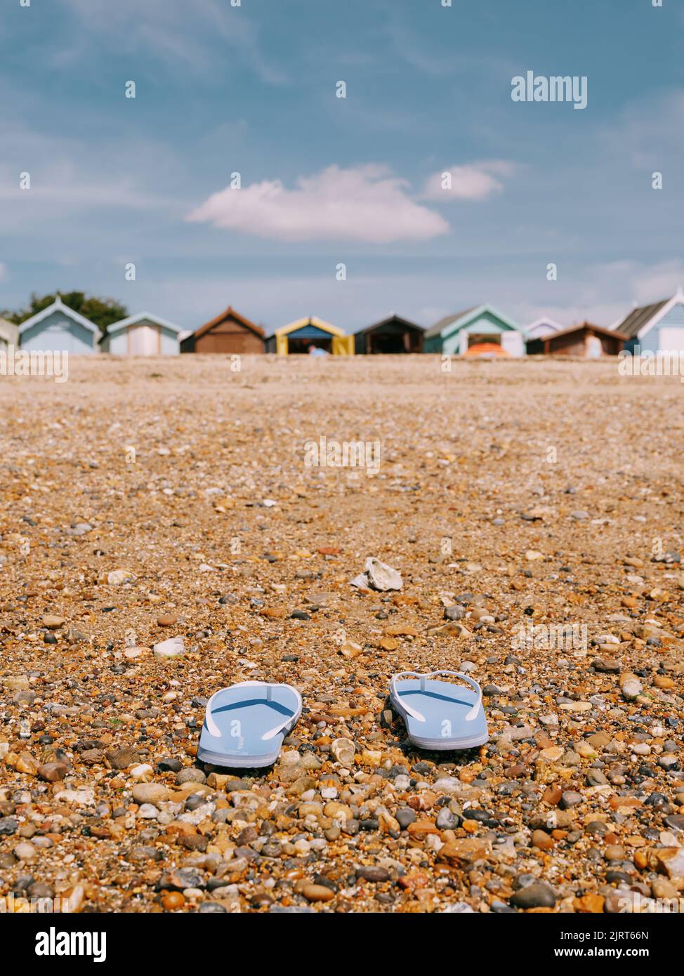 Blaue Flip Flops an einem Kiesstrand mit Strandhütten in West Mersea, Mersea Island, Essex, England - Sommeraufenthalt Badeurlaub Hintergrund Stockfoto