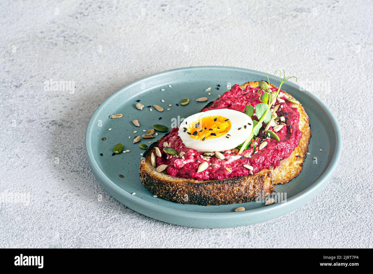 Vollkorn-Toast mit Rübenhummus, Samen, Ei und Mikrogemüse (gekeimt Erbsensprossen) auf hellgrauem Hintergrund. Das Konzept der gesunden Ernährung.. Stockfoto