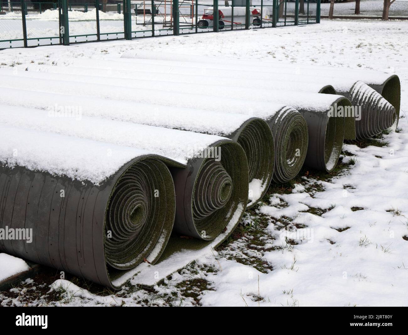 Mit Schnee bedeckte Rollen von Kunstgras warten auf die Zeit. Kunstrasen für Sportplätze und Stadien im Freien Stockfoto