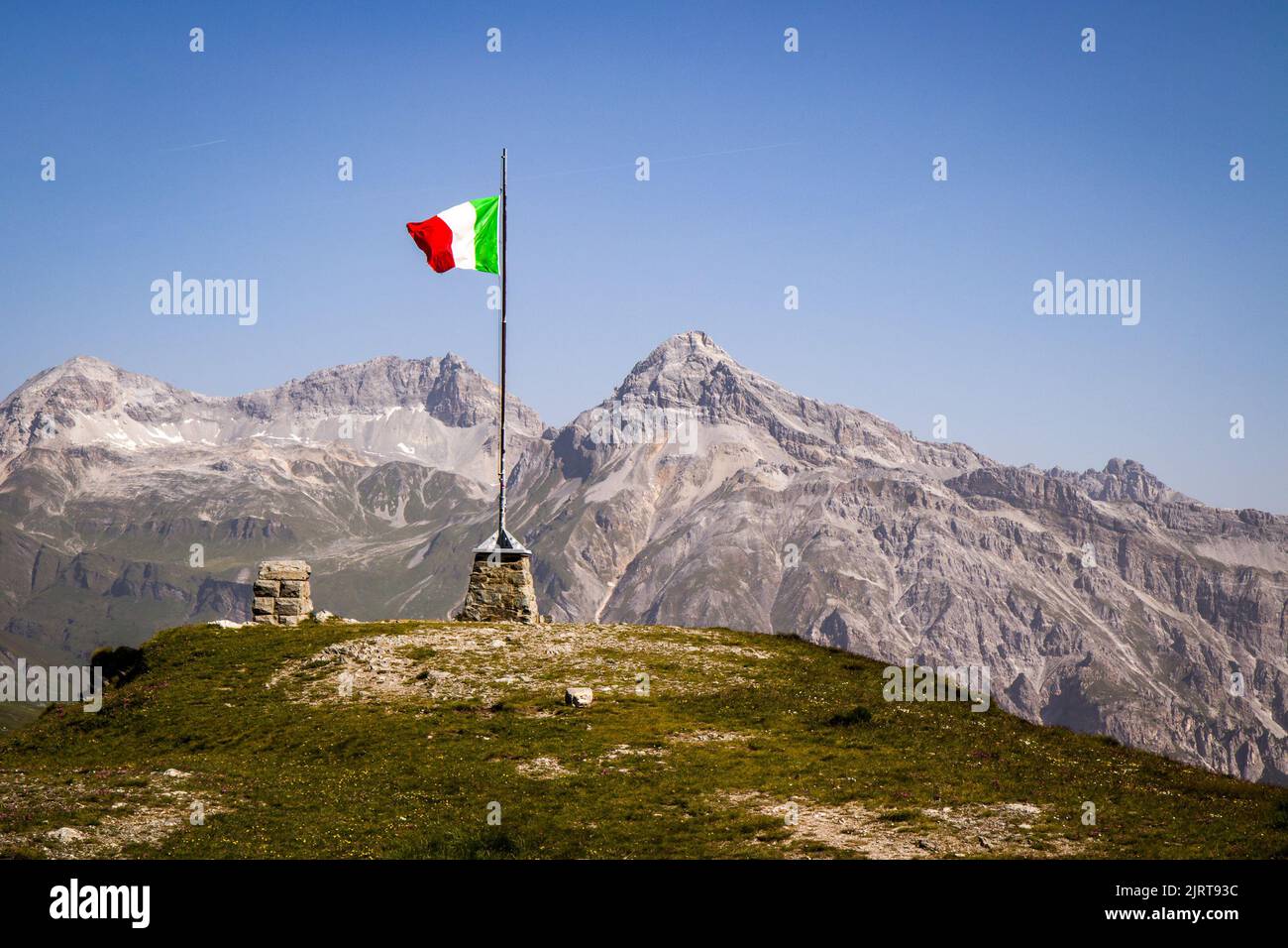 Schwenkende italienische Flagge im Pass (Teurihorn, Alperschallihorn und blauer Himmel ohne Wolken im Hintergrund) in der Nähe der Schweizer Grenze, Italien, Europa. H Stockfoto