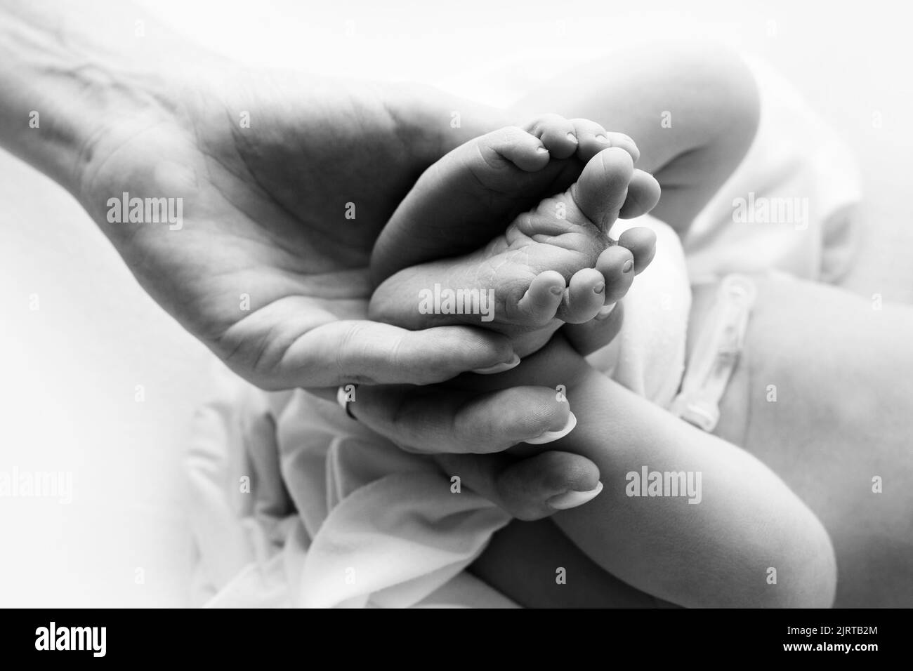 Hände der Eltern. Die Beine, die Füße des Neugeborenen in den Händen von Mama und Papa. Stockfoto