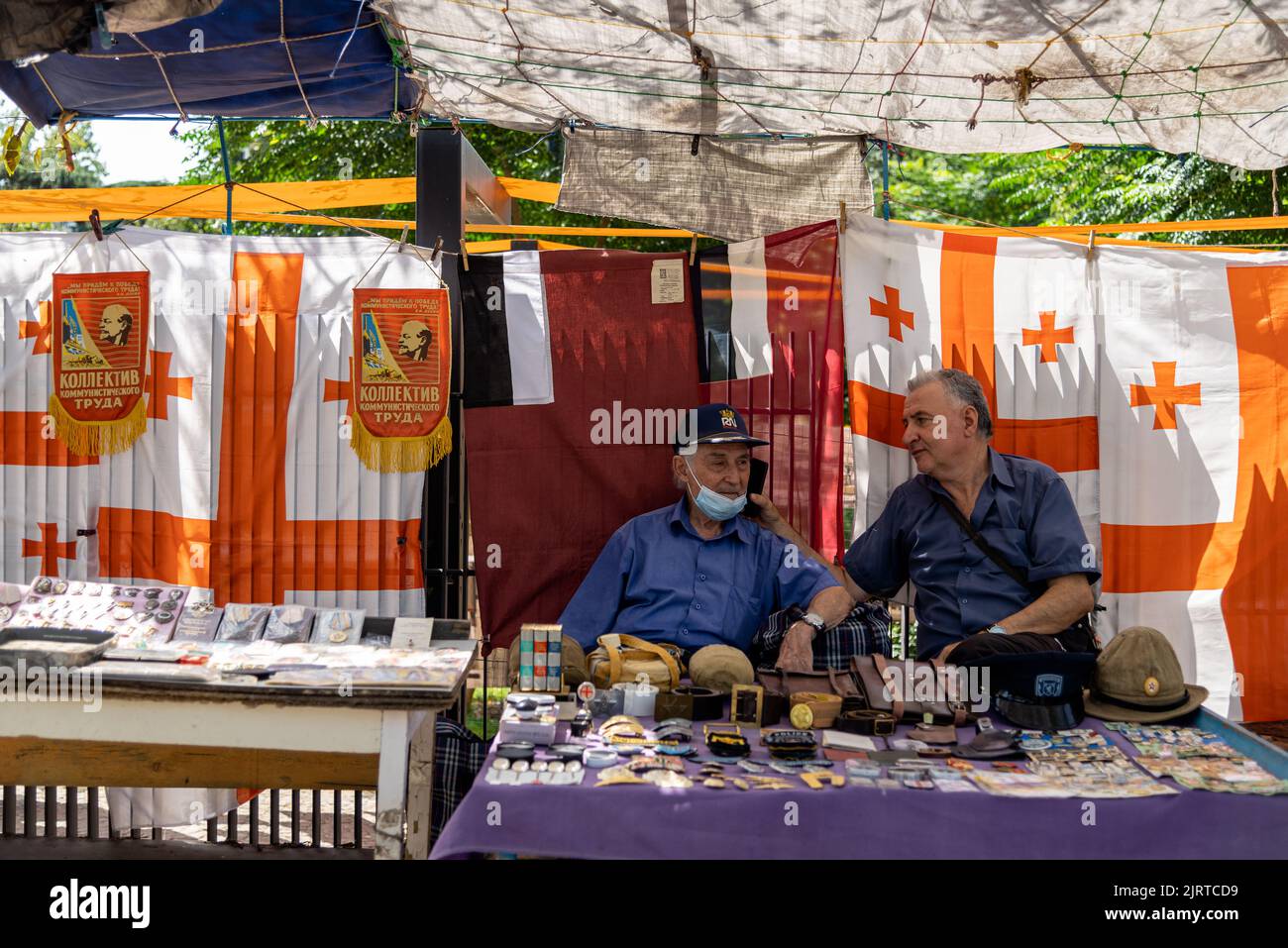 Zwei Männerverkäufer plaudern auf dem Flohmarkt in Tiflis mit georgischer Flagge im Hintergrund Stockfoto