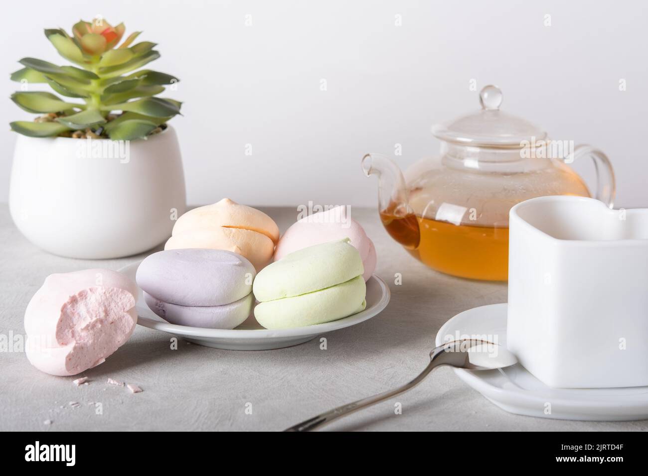 Teezeit. Eine gebissene Marschmalbe, eine Torte, eine Blume und transparente Gläser für eine Teezeremonie auf hellem Hintergrund. Teezeremonie. Frühstück. Stockfoto