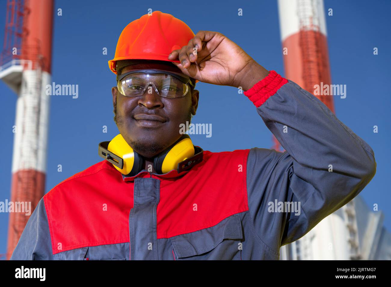 Portrait Des Schwarzen Kraftwerksarbeiters Mit Rotem Helm, Schutzbrille, Gehörschutzausrüstung Und Arbeitskleidung. Stockfoto