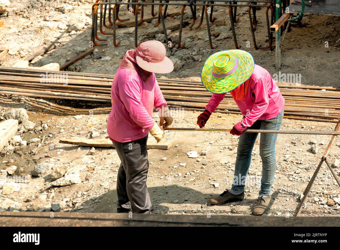 Zwei Bauarbeiter messen und markieren an einem sehr heißen Tag verformte Stäbe für die Fundamentstahlarbeiten. Stockfoto