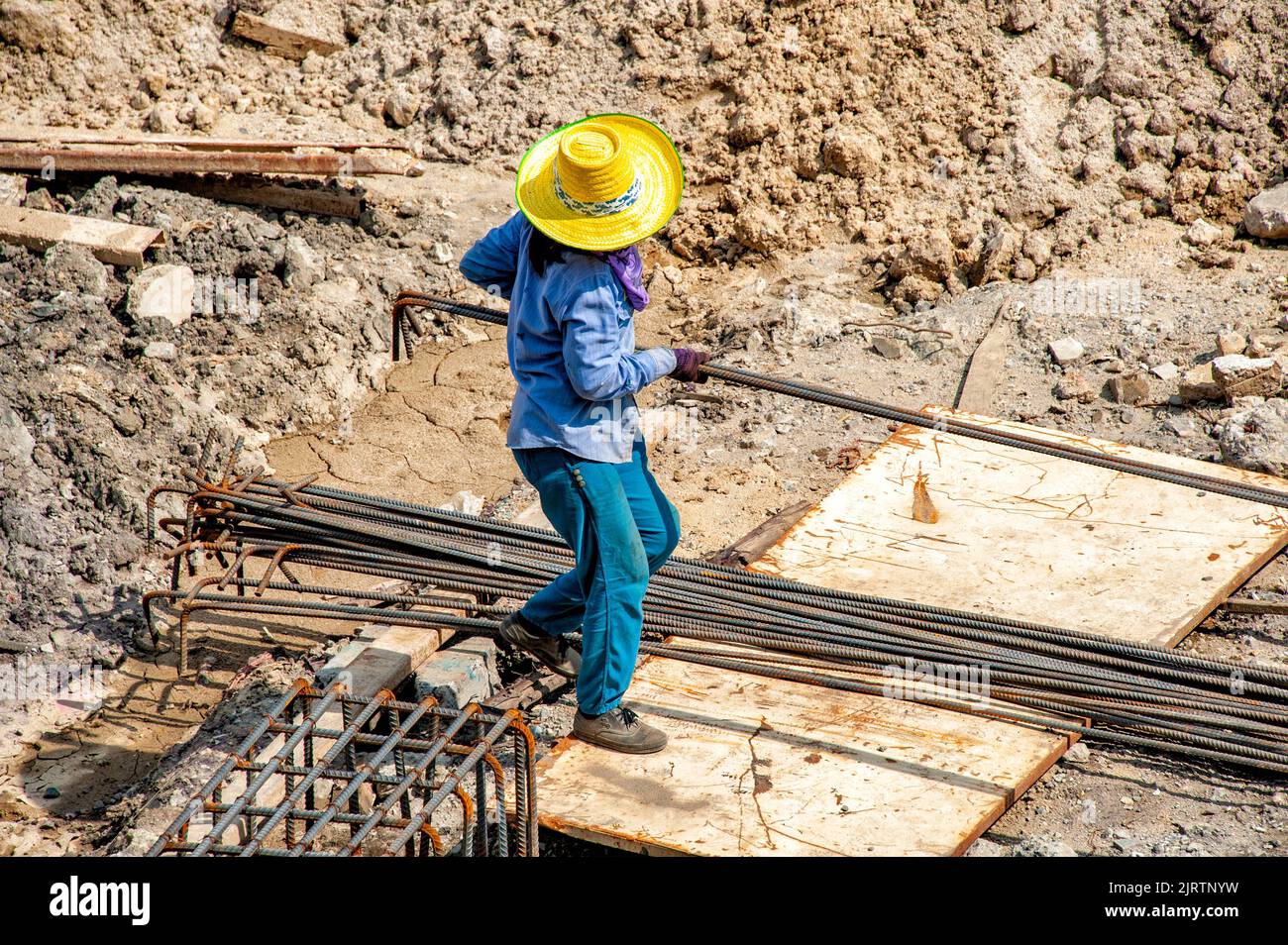 Ein Bauarbeiter trägt an einem sehr heißen Tag verformte Stäbe für die Fundamentstahlarbeiten. Stockfoto