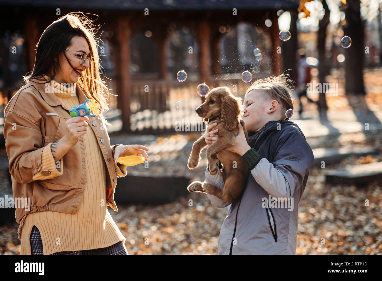 Glückliche Familie Mutter und Teenager Junge Sohn mit niedlichen Cocker Spaniel Welpen blasen Seifenblasen im Freien im Herbst Park. Stockfoto