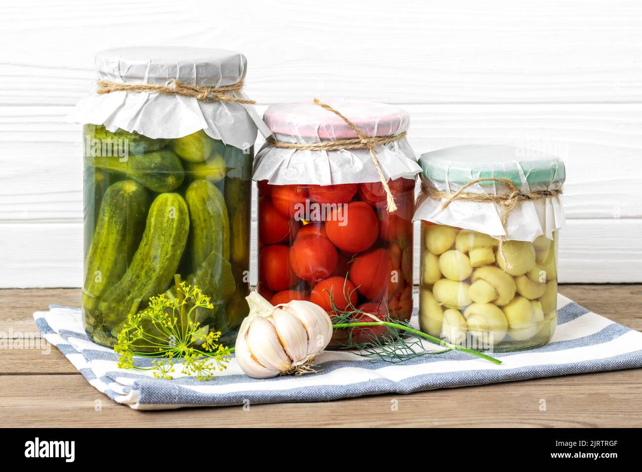Hausgemachte eingelegte Kirschtomaten, Gurken, Champignons, Knoblauch, Auberginen, Rote Paprika in Gläsern auf Holzregal hausgemachte Konserven und fermentierte Lebensmittel Konzept Saisonprodukt. Stockfoto