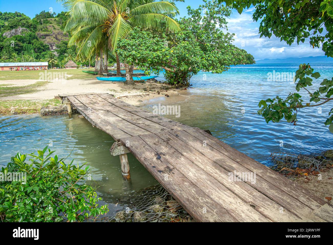 Eine kleine hölzerne Plattform überquert einen kleinen Bach, der in einer kleinen Inselstadt in Fidschi zum Meer führt. Stockfoto