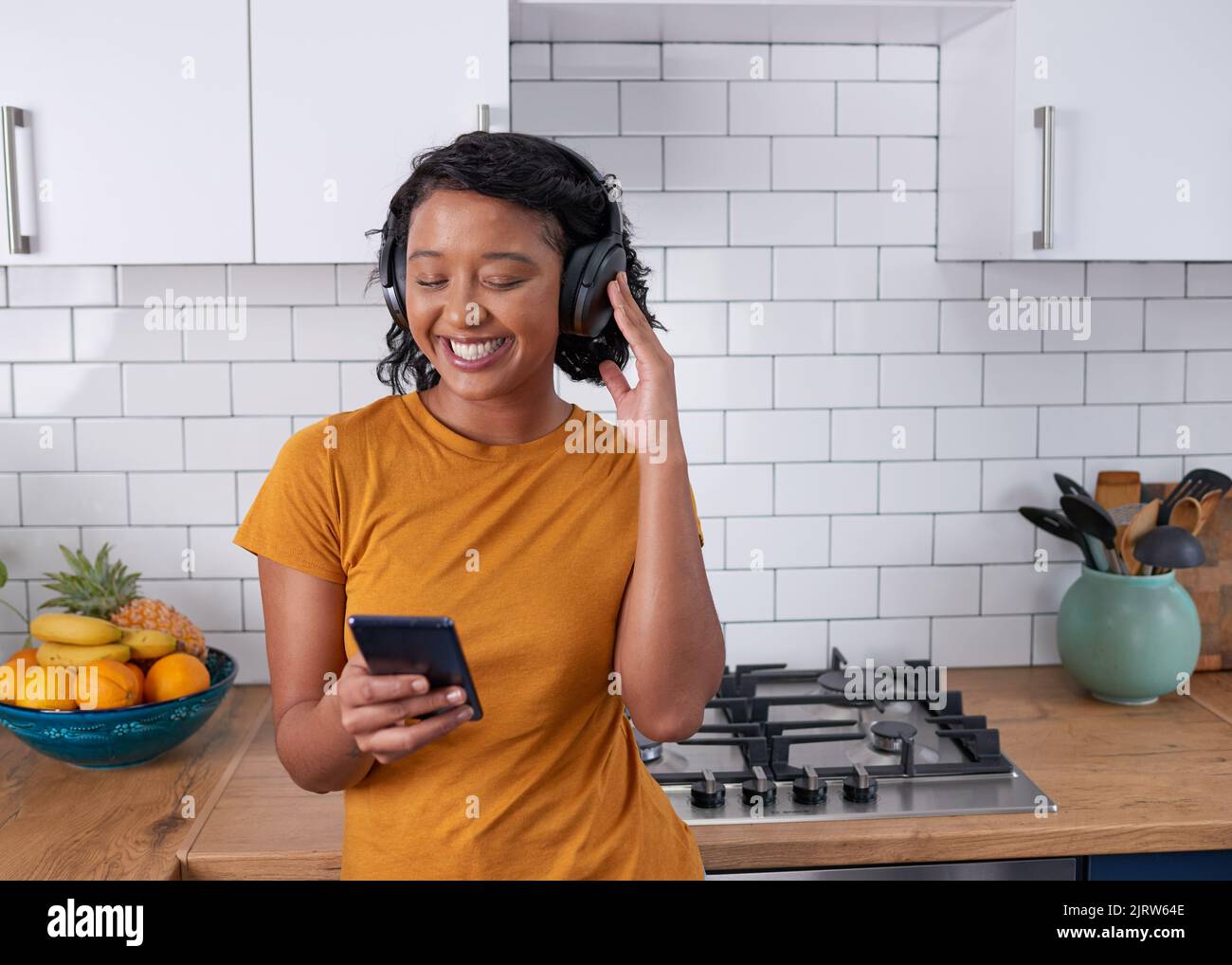 Eine junge Frau streamt Musik in ihrer Küche über Kopfhörer Stockfoto