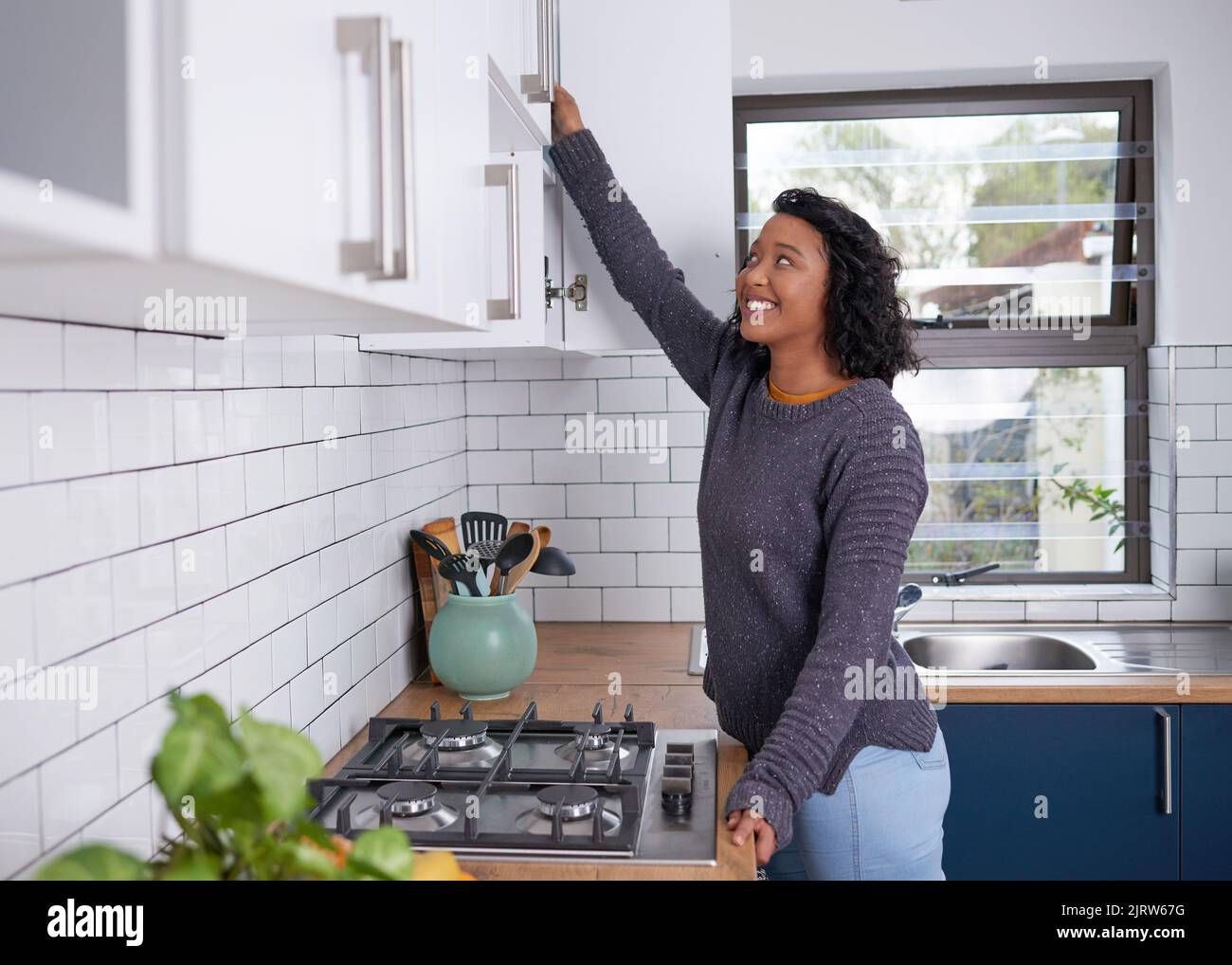 Eine junge, multiethnische Frau greift in ihre Küchenschränke Stockfoto