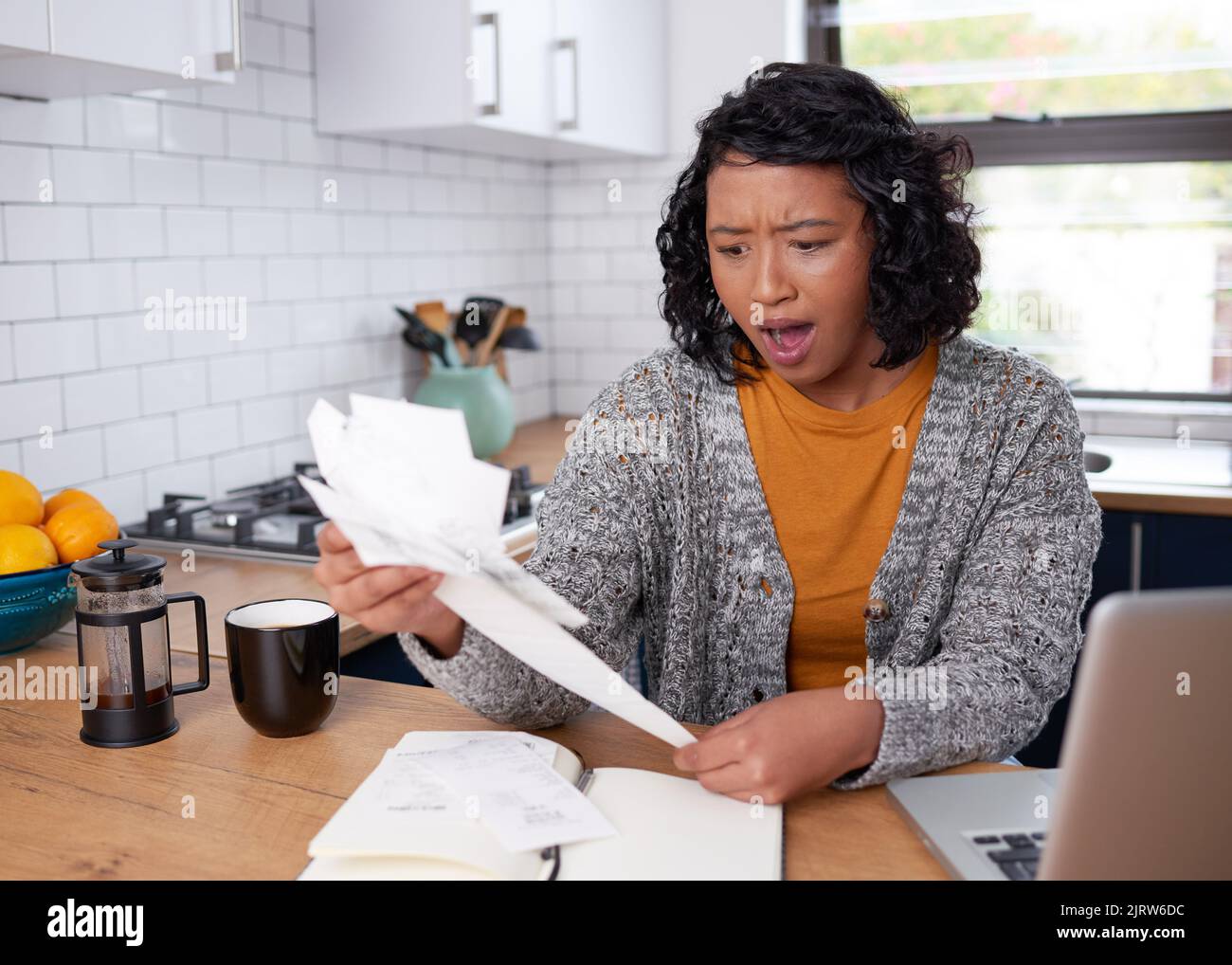 Eine junge, multiethnische Frau ist schockiert, wenn sie die Rechnungen für Haushaltsausgaben überprüft Stockfoto