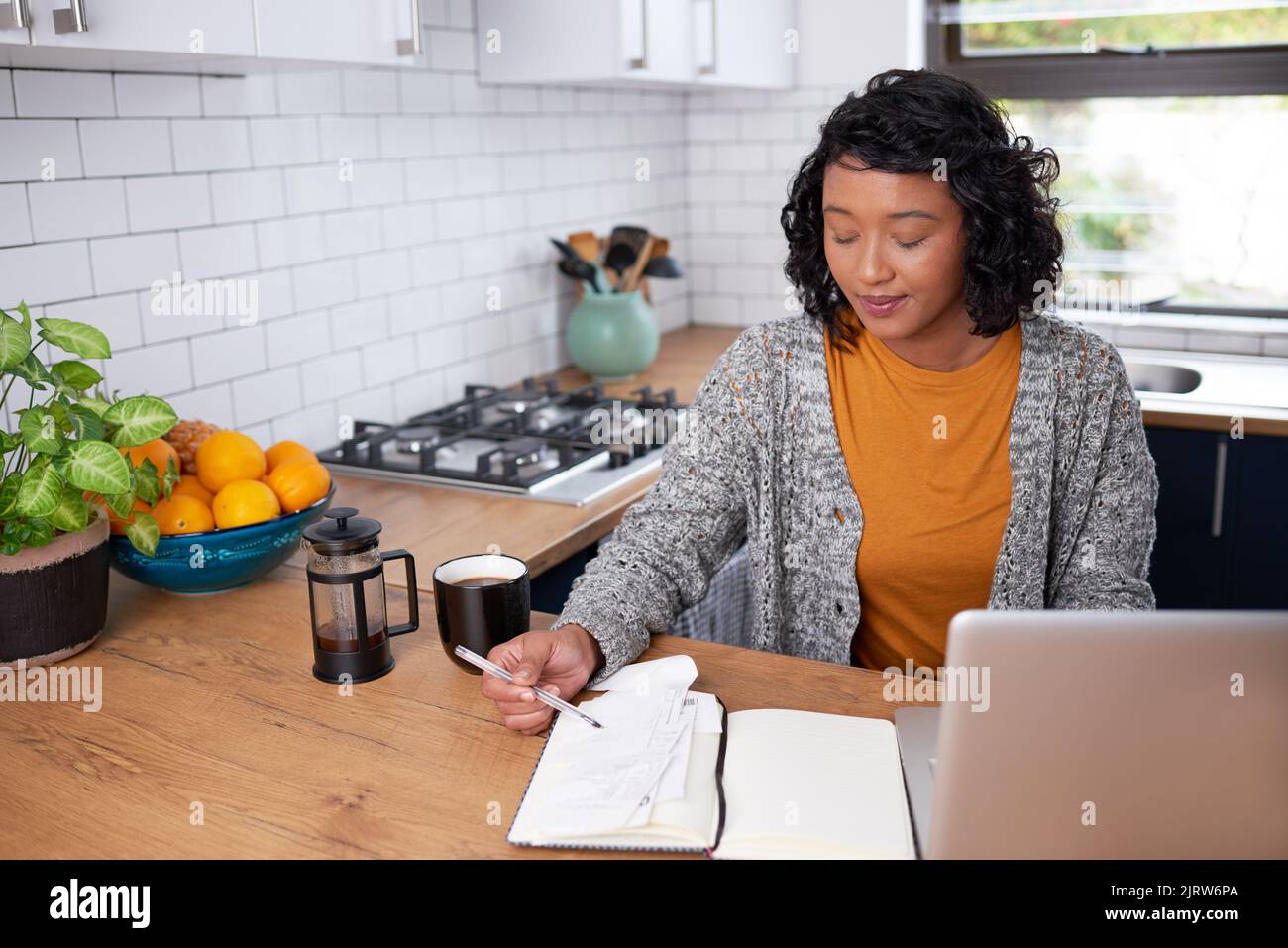 Eine junge, multiethnische Frau überprüft ihre Haushaltsfinanzen in der Küche Stockfoto