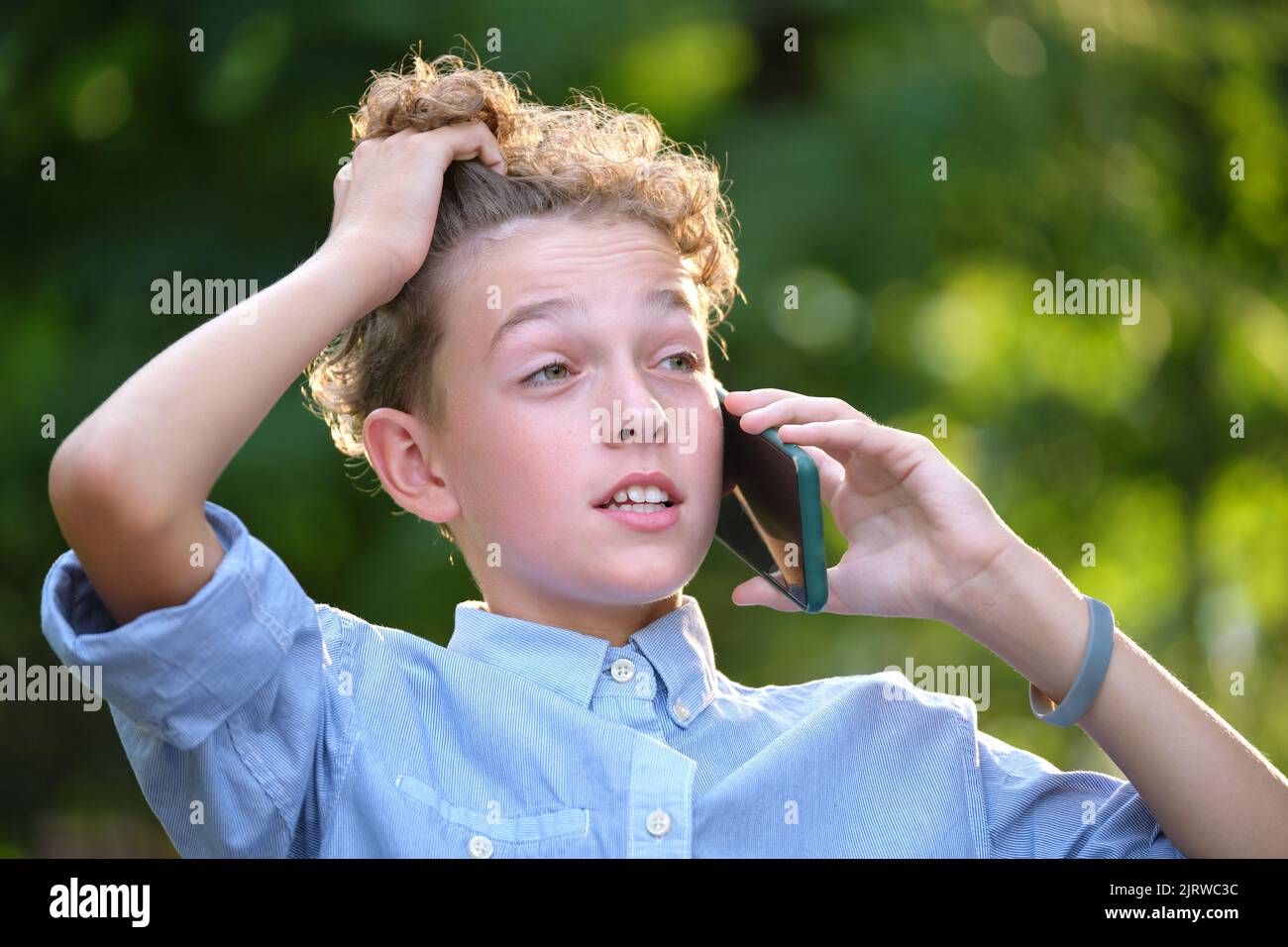 Kleiner Junge, der im Sommerpark mit dem Handy im Gespräch ist. Konfliktsituationen im Teenageralter Konzept Stockfoto