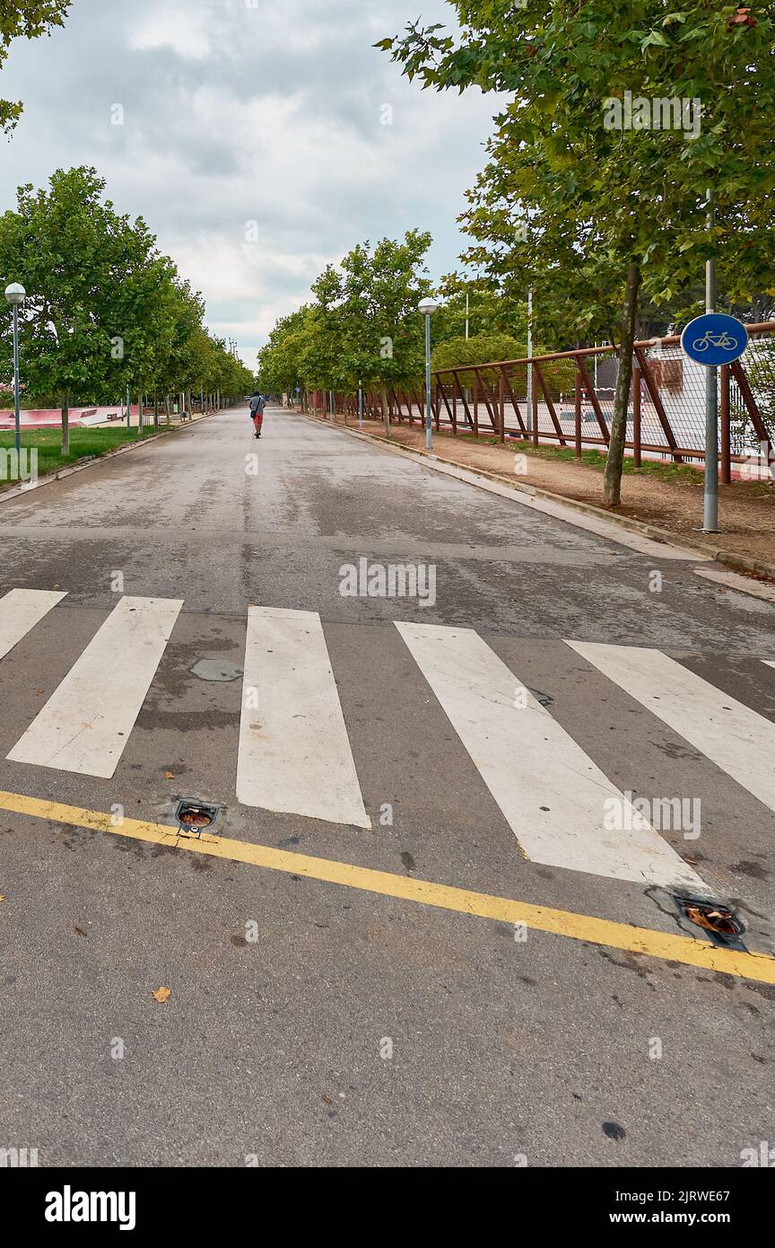 Crosswalk im Vordergrund mit einer Person auf einem Roller im Hintergrund. Stockfoto