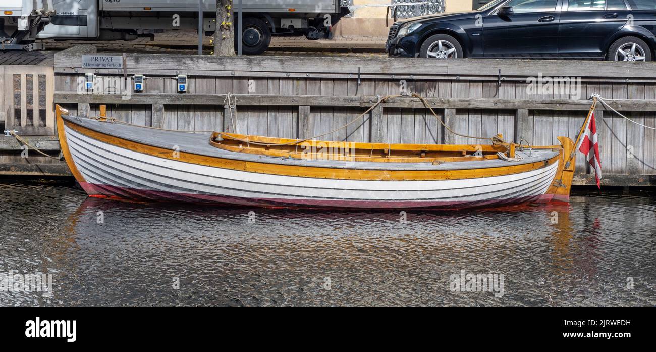 Elegantes Segelboot aus Holz mit der dänischen Flagge, das auf einem Kanal in Kopenhagen festgemacht ist Stockfoto