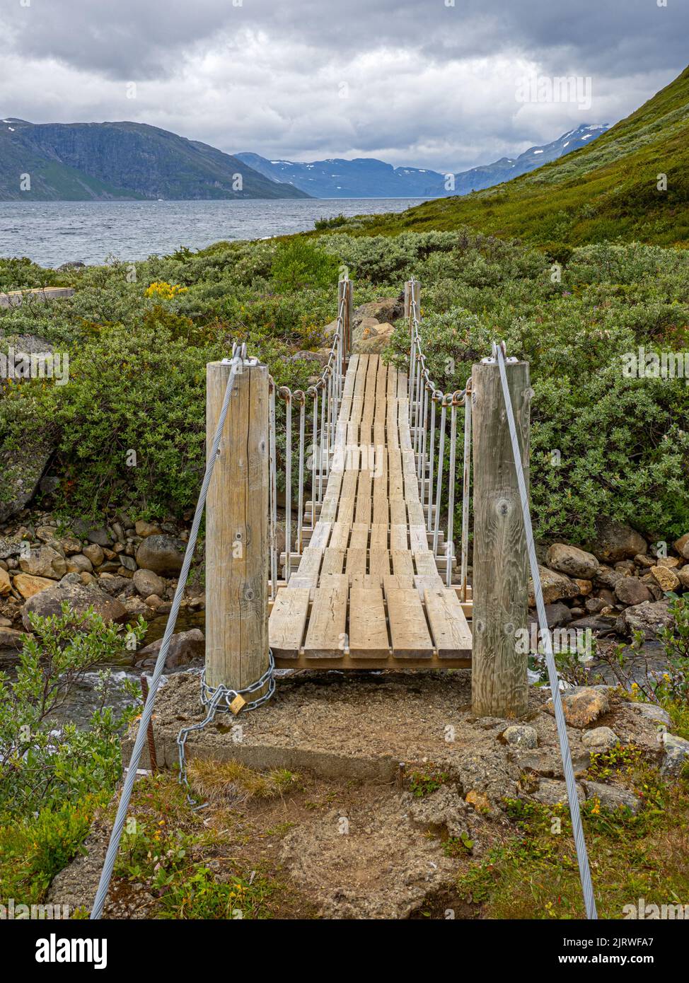 Kleine Hängebrücke über einen kleinen Bach auf einem Pfad entlang des Ufers des Bygdin-Sees im Jotunheimen-Nationalpark Norwegen Stockfoto
