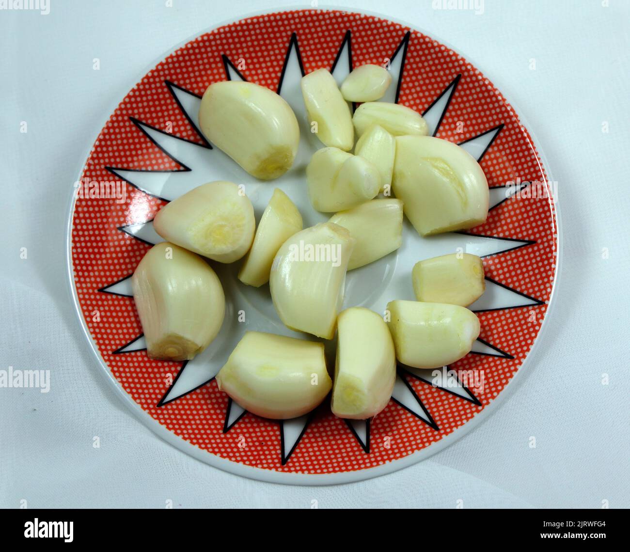 Ganze geschälte Knoblauchzehen auf einer hübschen Untertasse. Einrichtung von Studio Stockfoto