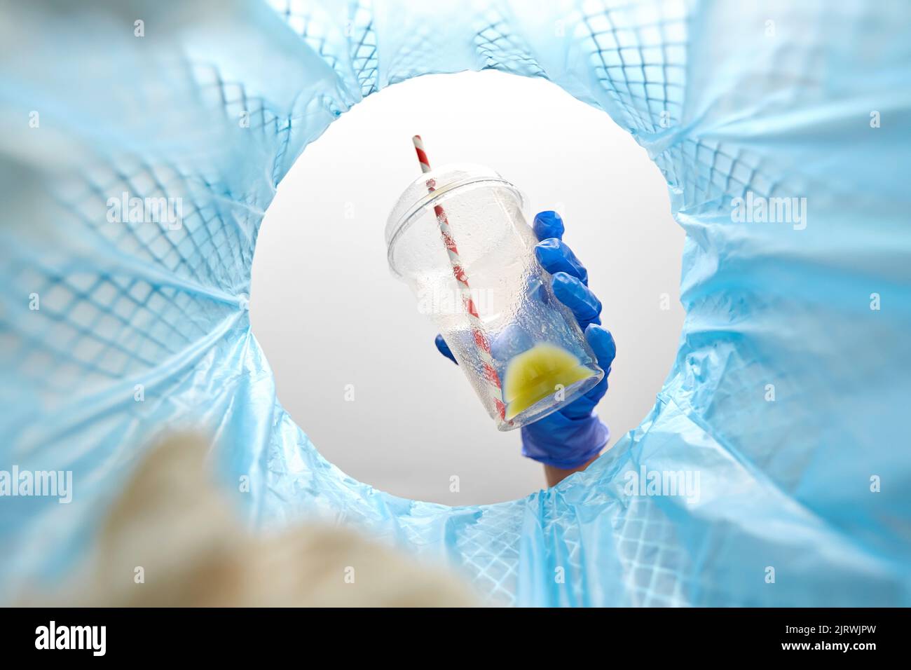 Hand in Handschuh werfen Plastikbecher in den Mülleimer Stockfoto