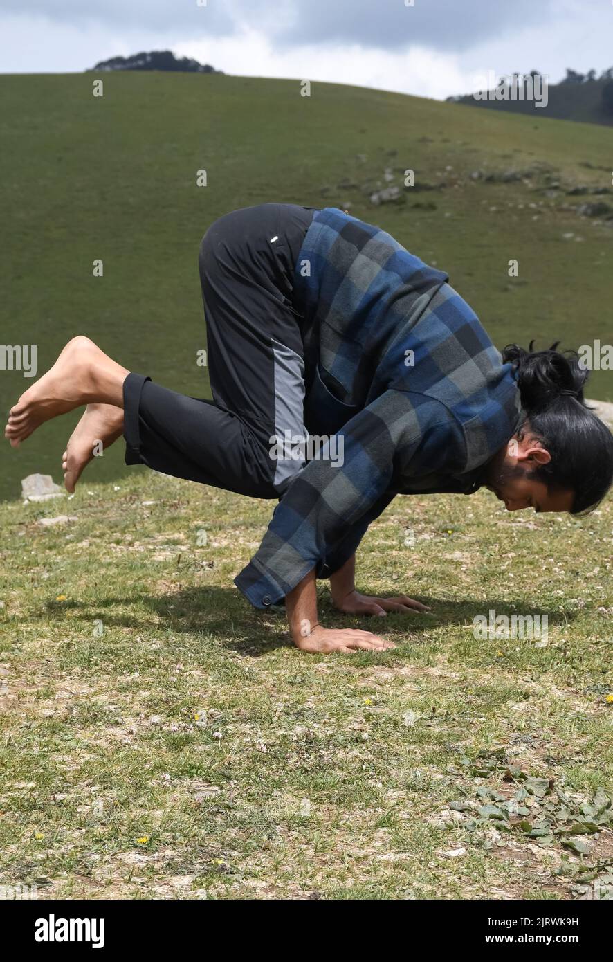 Ein junger Inder, der morgens im Berg die Bakasana Yoga-Pose (Krähenpose) praktiziert Stockfoto