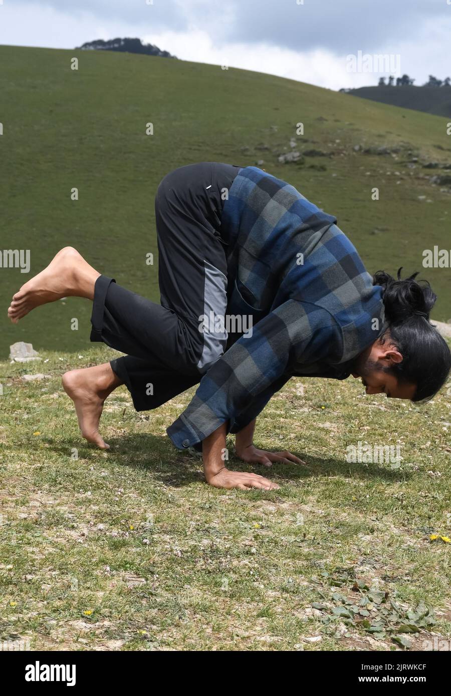 Ein junger Inder, der morgens im Berg die Bakasana Yoga-Pose (Krähenpose) praktiziert Stockfoto