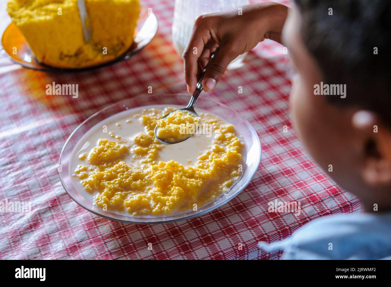 Brasilianisches Kind, das Mais Couscous mit Milch konsumiert. Beliebtes Gericht aus der nordöstlichen Region Brasiliens, weit verbreitet zum Frühstück verzehrt. Stockfoto