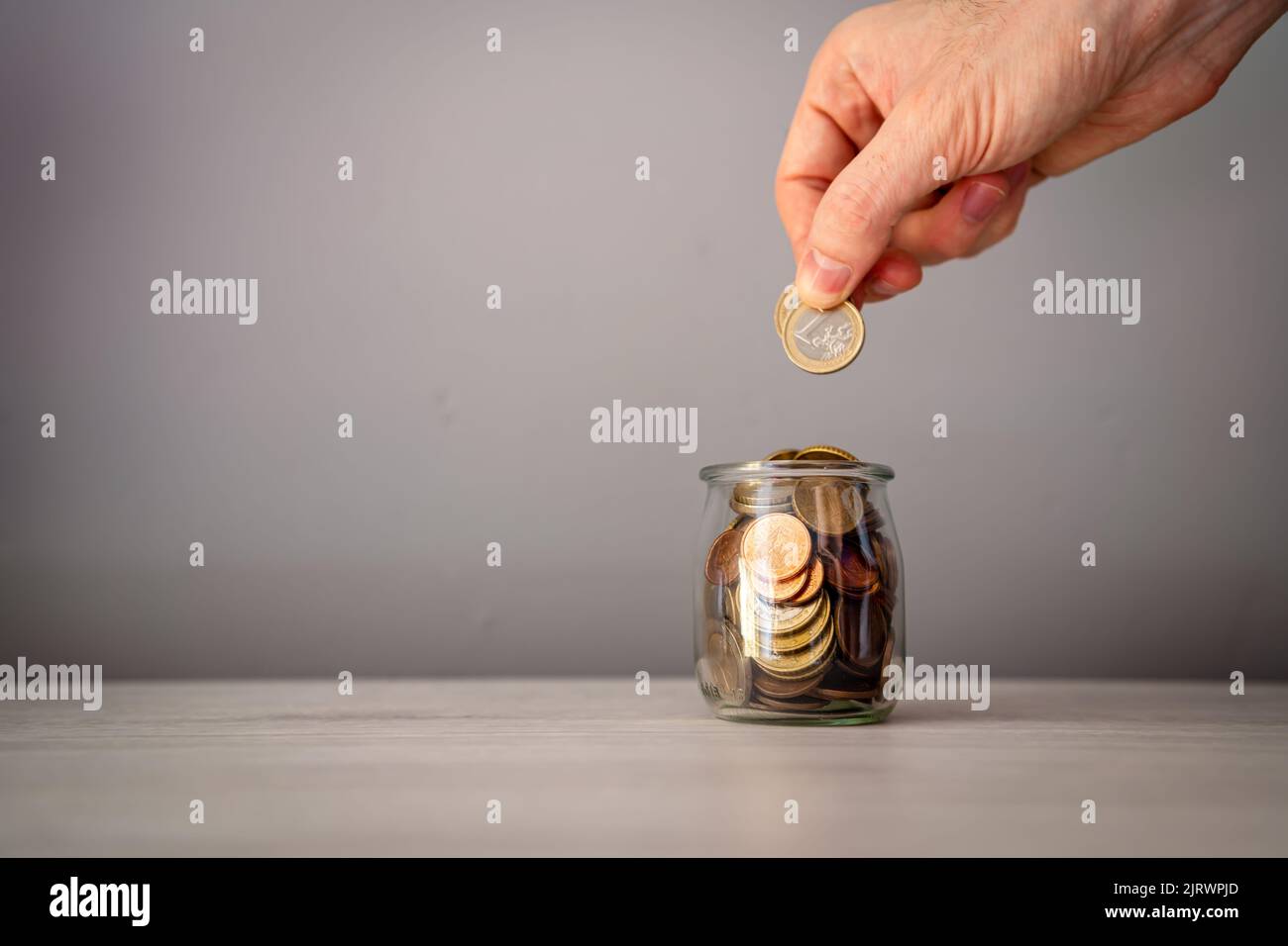 Man's Hand Hinzufügen von Münzen in einem Glas auf einem hellen Holztisch, zu speichern oder zu spenden. Geldkonzept. Stockfoto