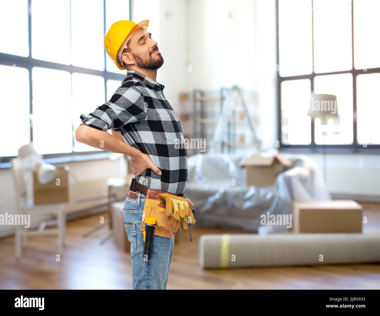 Männlicher Arbeiter oder Baumeister, der zu Hause Rückenschmerzen hat Stockfoto
