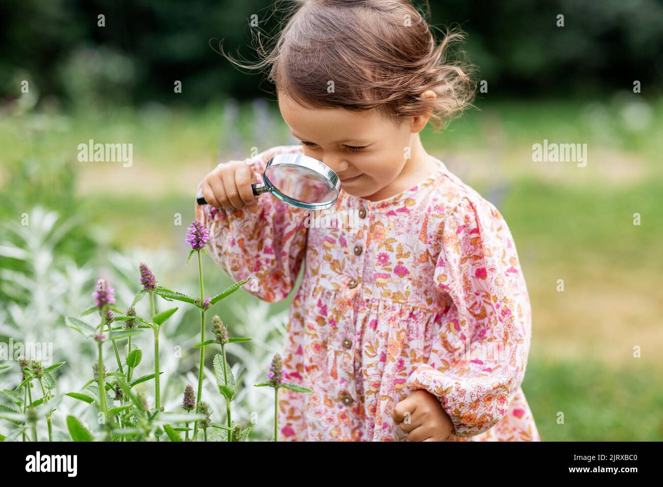 Baby Mädchen mit Lupe Blick auf Gartenblumen Stockfoto